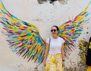 Sandra Hodes standing in front of a colorful wings mural